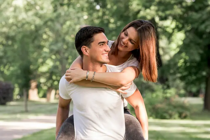 un chico cargando a su pareja, ellos estan muy enamorados paseando en un parque